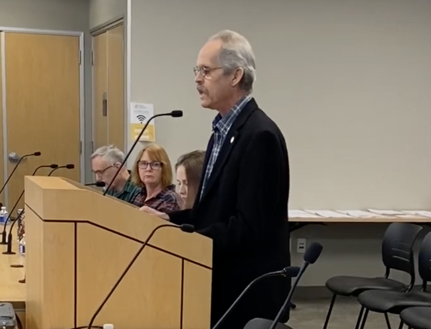 A man named Greg Rees standing at a podium, addressing a group of people.